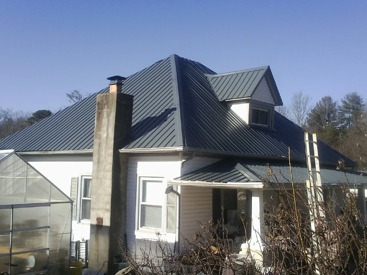 Dark blue standing seam metal roof on a white farmhouse with dormer — Slate & Tile Roof Repair by Roofing Brothers in Olivet