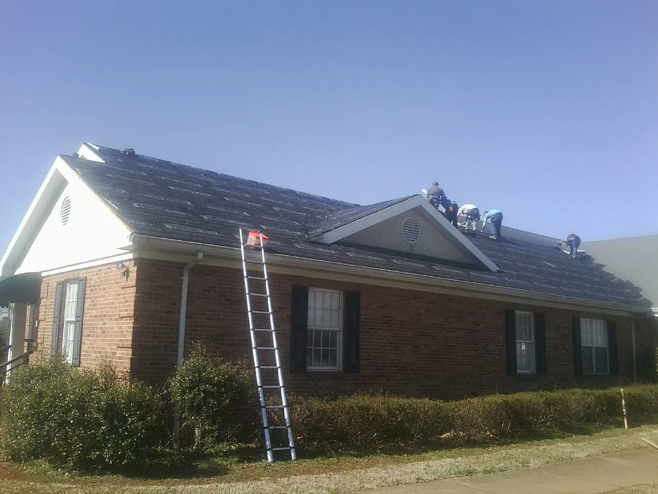 Crew tearing shingles off a brick ranch roof with a ladder set — Emergency Roof Repair work by our crew in Olivet