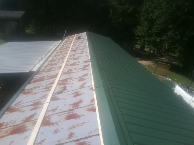 Old rusted panels beside newly installed green metal roofing — Wind Damage Roof Repair by Roofing Brothers in Olivet