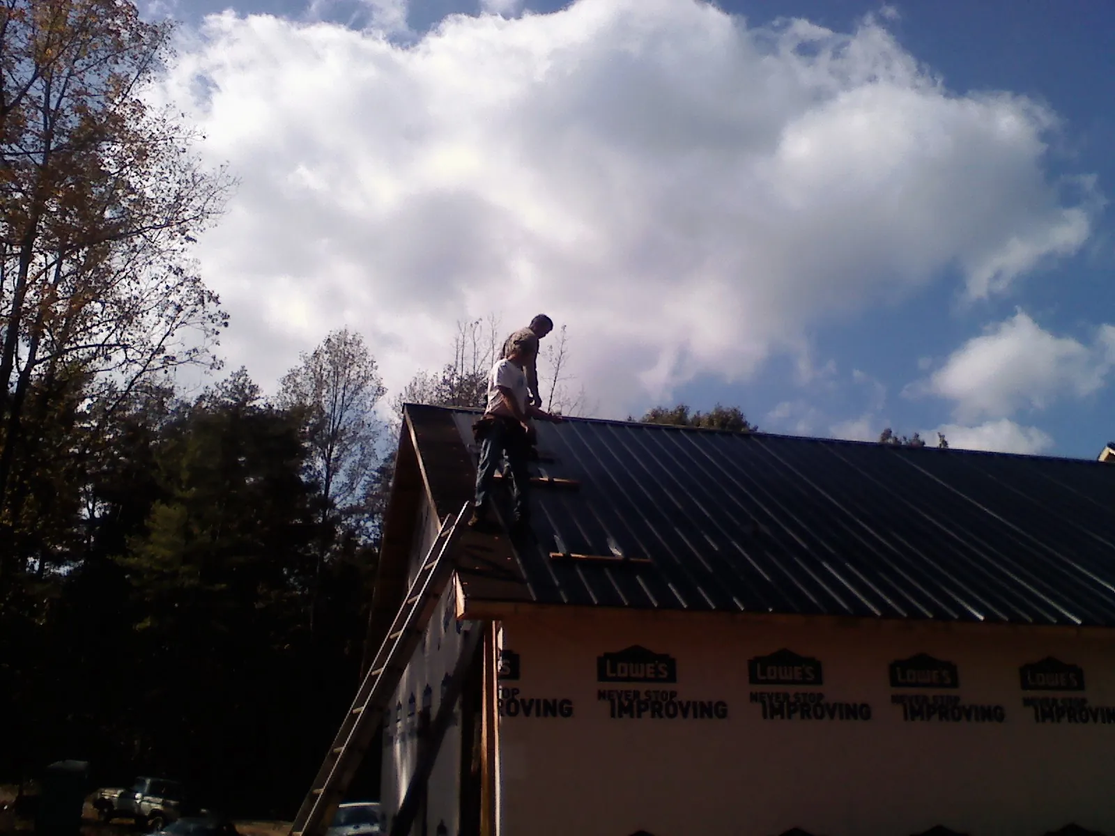 Roofer fastening dark metal panels high against a cloudy sky, from a Roof Inspection job in Olivet